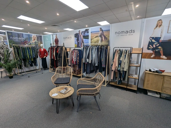exhibition stand with fibreboard prints on aluvision frames with racks of womens clothes in front, plus two chairs and a table