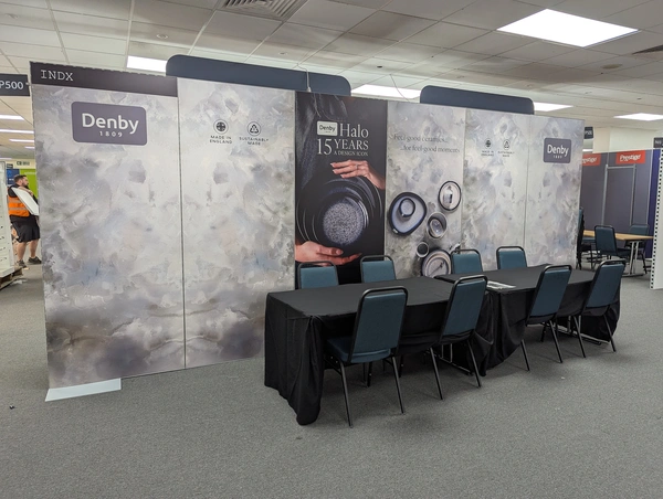 a 6m wide wall with printed graphic panels for denby pottery, with a table and chairs in front in an exhibition hall
